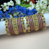 Decorative gold and red bangles on a white arm with flowers in the background