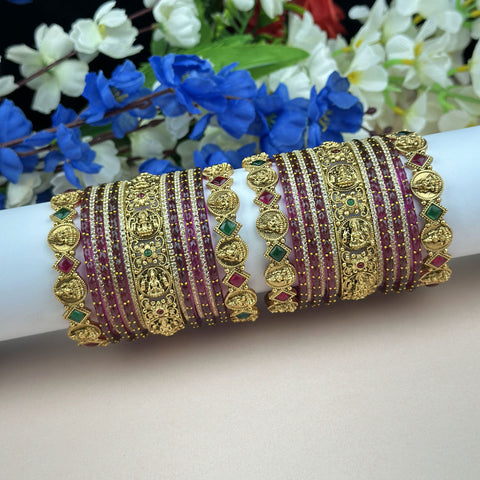 Decorative gold and red bangles on a white arm with flowers in the background