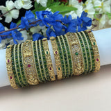 Decorative bangles with green stones and gold accents on a white arm against a floral background.