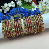 Decorative gold and red bangles on a white surface with flowers in the background