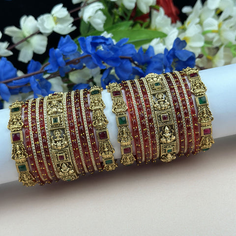 Decorative gold and red bangles on a white surface with flowers in the background