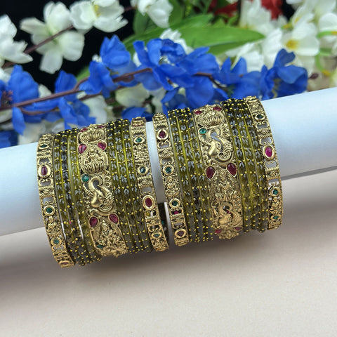 Decorative gold bangles with gemstones on a white surface with flowers in the background