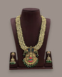 Gold-toned traditional Indian jewelry set displayed on a dark brown jewelry bust, including a multi-strand necklace with a large ornate pendant and matching drop earrings, featuring green and red stone accents.