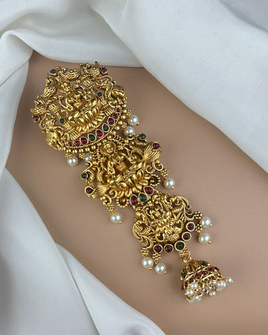 Gold bracelet with intricate design and pearls on a white fabric background