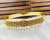 Gold belt with intricate designs and red stones on a white cushion with wooden background