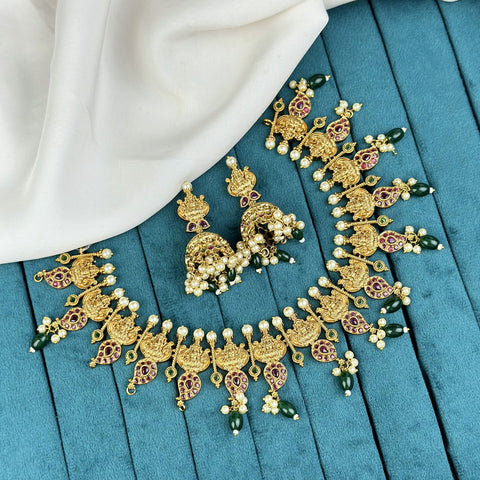 Ornate gold necklace with green and red accents on a blue fabric background