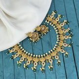 Ornate gold necklace with green beads on a blue fabric background