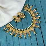 Gold necklace with green and red accents on a blue fabric background
