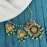Ornate gold necklace with green beads on a teal surface