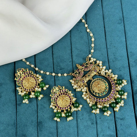 Ornate gold necklace with green beads on a teal surface