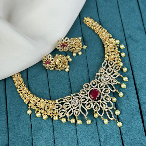 Gold necklace with red gemstone and pearl earrings on a teal surface