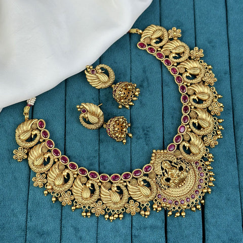 Gold necklace with red gemstones and matching earrings on a blue fabric background