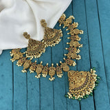 Ornate gold necklace with green stones on a blue fabric background
