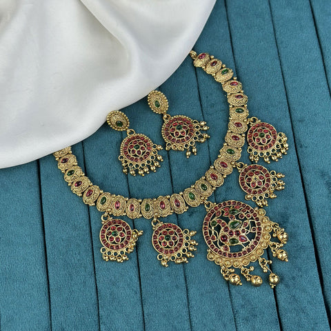 Ornate gold necklace with red and green gemstones on a blue fabric background