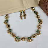 Gold necklace with green stones and matching earrings on a white surface.
