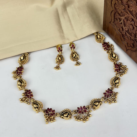 Gold necklace and earrings with red stones on a white surface