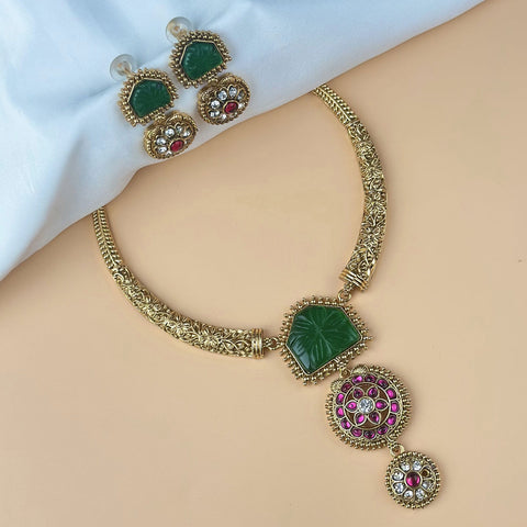 Gold necklace with green and red gemstones on a mannequin, with earrings in the background.