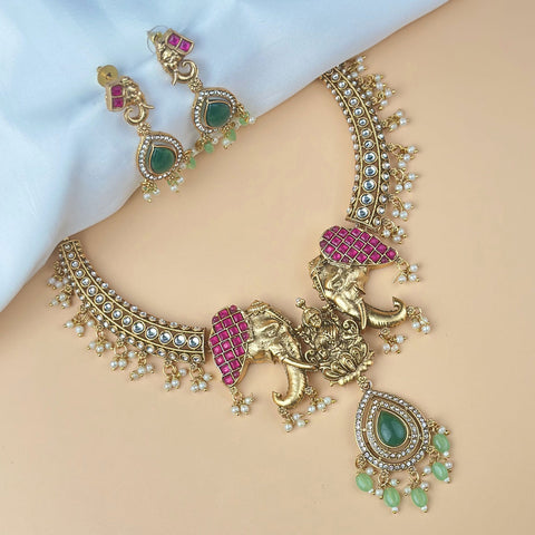 Ornate gold necklace with pink and green accents on a person's neck, with matching earrings.
