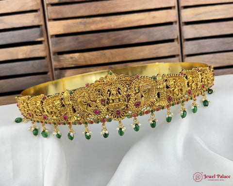 Gold necklace with green and red stones on a white surface with wooden background