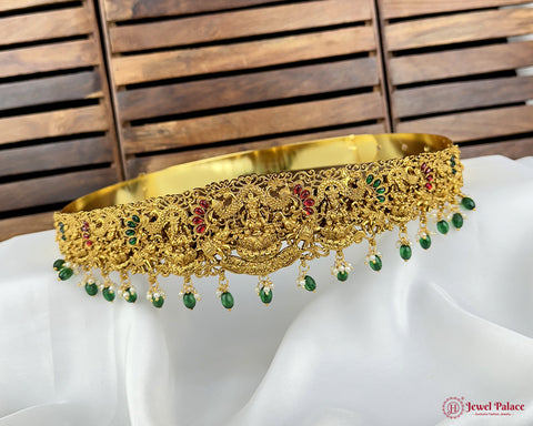 Gold necklace with green and red stones on a white fabric background