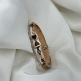 Rose gold bracelet with heart and diamond details on a white fabric background