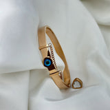 Gold bracelet with a blue eye charm on a white fabric background