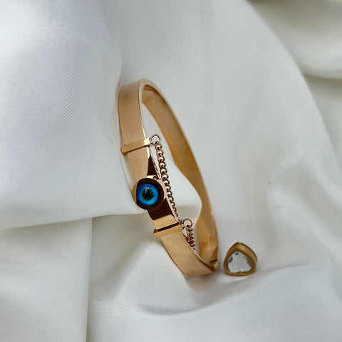 Gold bracelet with a blue eye charm on a white fabric background