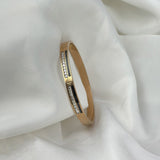 Gold bracelet with embedded diamonds on a white fabric background