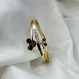 Gold bracelet with black clover and diamond accents on a white fabric background