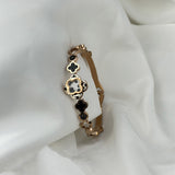 Gold bracelet with black clover-shaped charms on a white fabric background