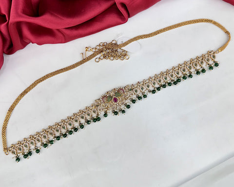 Decorative necklace with green beads and gold chain on a white surface