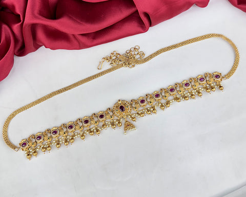 Gold necklace with red stones on a white surface with red fabric in the background