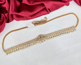 Gold necklace with gemstones on a white surface with red fabric in the background