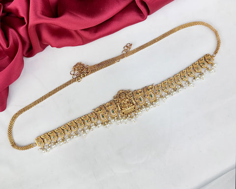 Gold necklace with intricate designs on a white surface with red fabric in the background