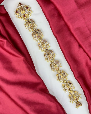 Decorative gold embroidery on a white fabric strip against a red satin background