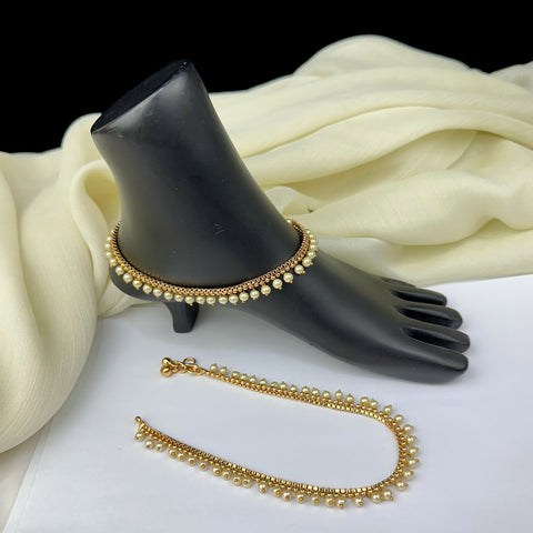 Gold anklets on a black foot-shaped stand with white fabric background