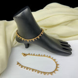 Gold anklets on a black mannequin foot with a white fabric background