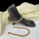 Gold anklets on a black mannequin foot with white fabric background