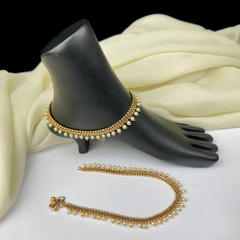 Gold anklets on a black mannequin foot with white fabric background