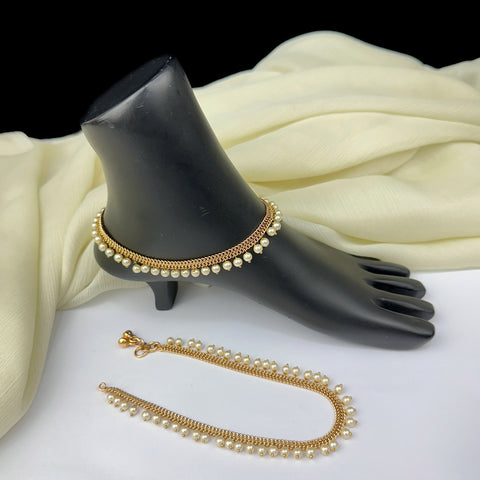 Gold anklets with pearls on a black mannequin foot and white fabric background