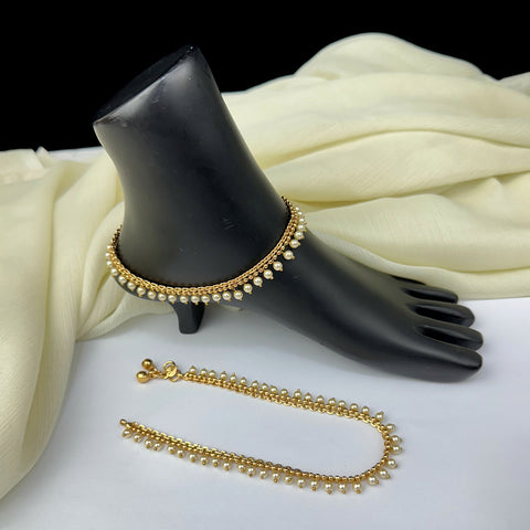 Gold anklets on a black mannequin foot with white fabric background