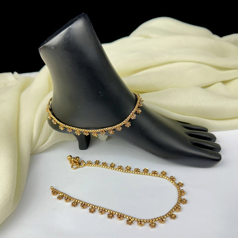 Gold anklets on a black mannequin foot with white fabric background