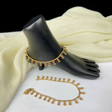 Gold anklets on a black mannequin foot with white fabric background