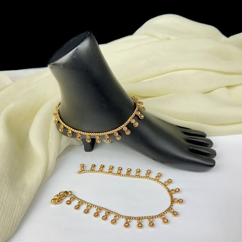 Gold anklets on a black mannequin foot with white fabric background