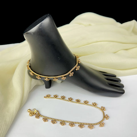 Gold anklets on a black shoe mannequin with a white fabric background