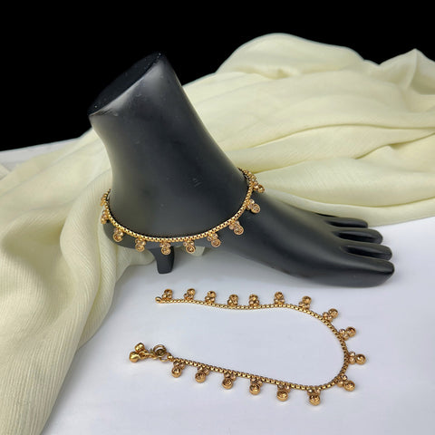 Gold anklets on a black mannequin foot with a white fabric background