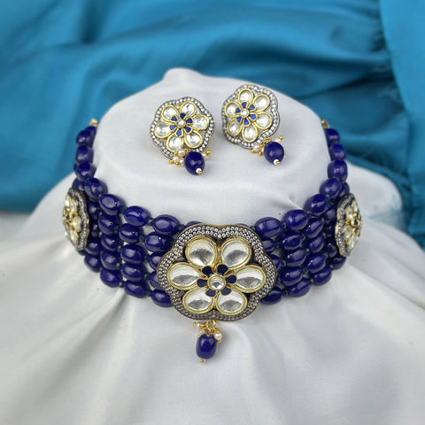 Jewelry set with a blue beaded necklace and matching earrings on a white cushion with a blue fabric background.