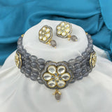 Gray beaded necklace with gold floral designs on a white cushion against a blue fabric background