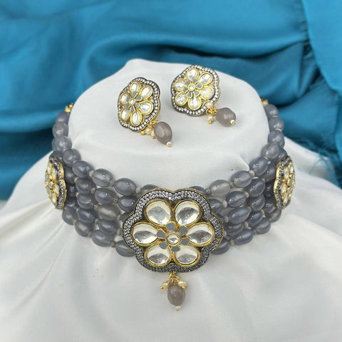 Gray beaded necklace with gold floral designs on a white cushion against a blue fabric background