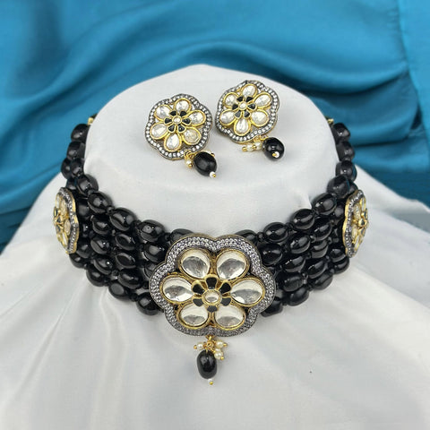 Black beaded necklace with floral gold and white accents on a white stand against a blue fabric background